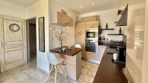 A compact kitchen with modern appliances, a dining area with a chair, and a small island with decorative plants. - 2-room apartment in Porticcio with air conditioning and parking (Porticcio)