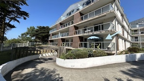 Un edificio residencial de varios pisos con balcones, una entrada curva y un área cercada con vegetación.