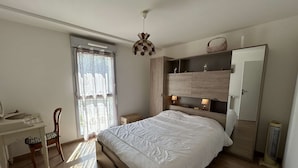 Un dormitorio con cama, escritorio, silla, armario y ventana con cortinas.