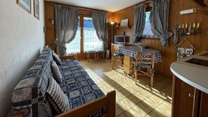 Una habitación acogedora con sofá, una mesita con televisor y una zona de cocina con fregadero y utensilios.