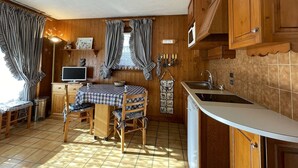 Una cocina acogedora con armarios de madera, una mesa de comedor con mantel a cuadros y un fregadero.