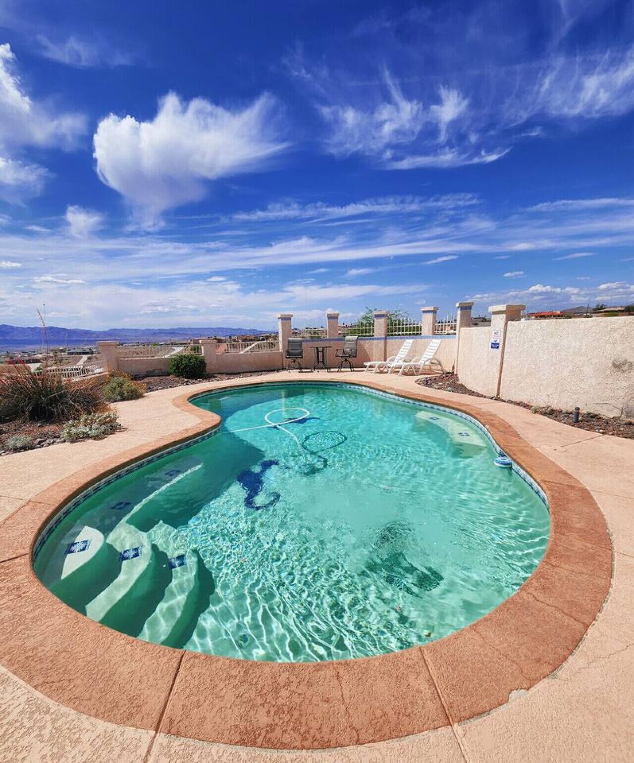 Une piscine au design incurvé, entourée d’un petit muret et surplombée par un ciel bleu clair.