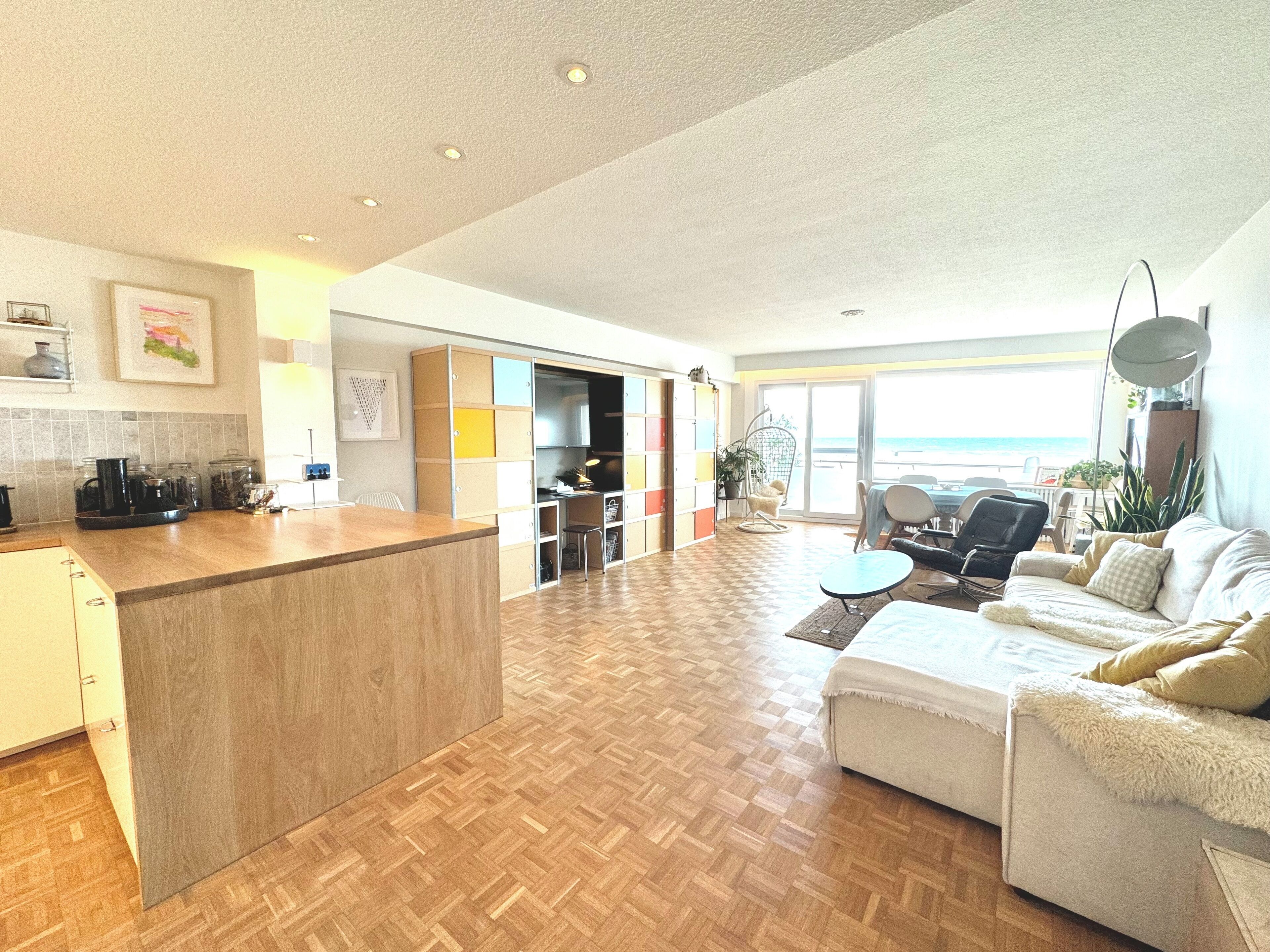 Un espacio habitable amplio con piso de madera, un sofá, una mesa de comedor y una cocina con mostrador y armarios.