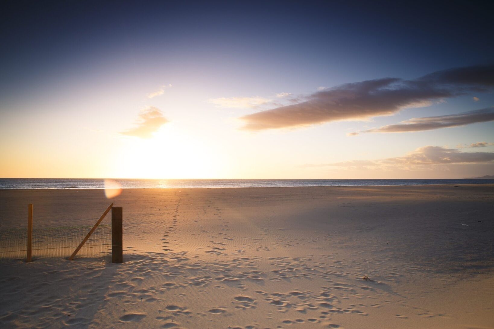 A beach with footprints leading to a fence.