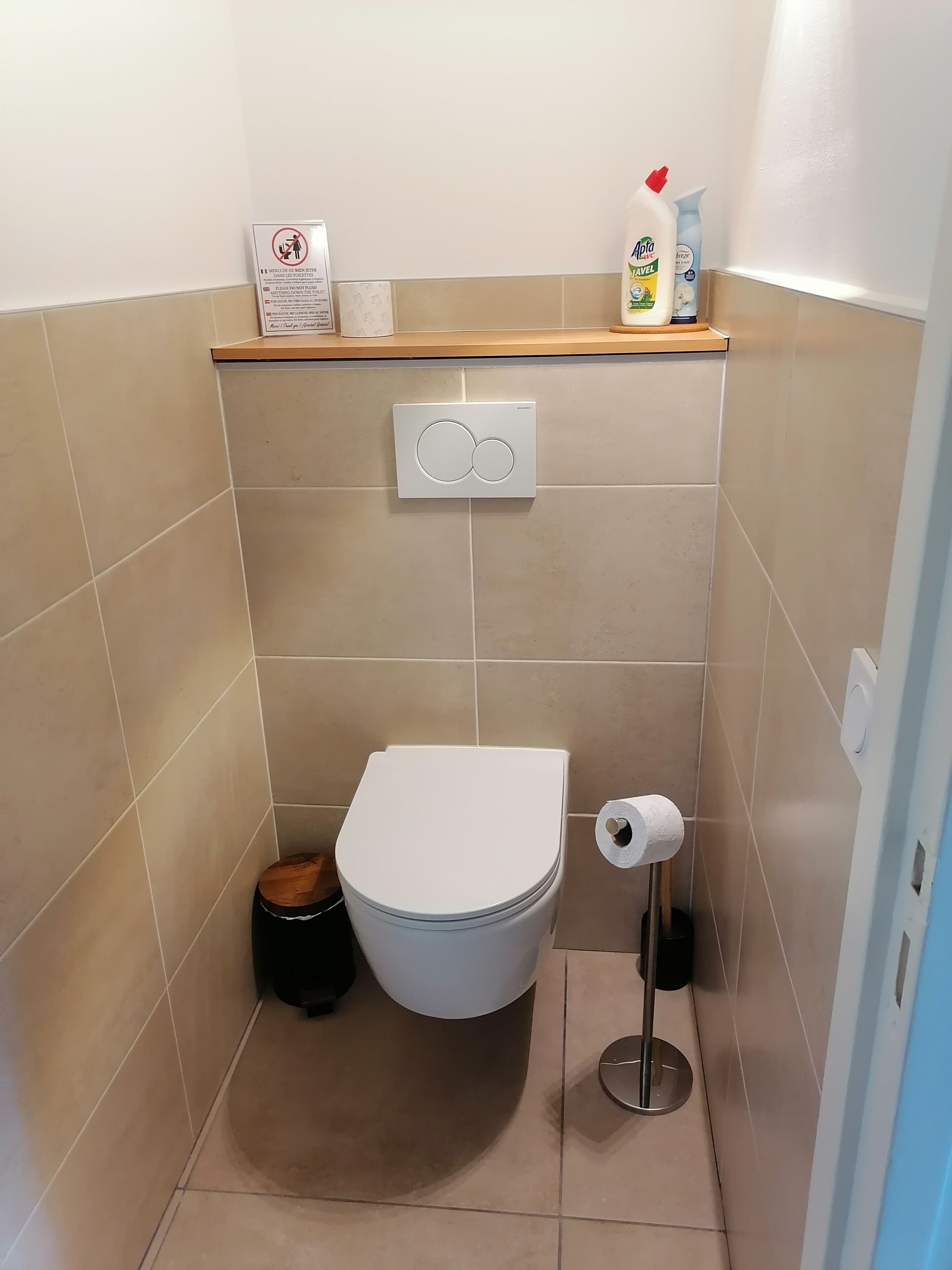 A small bathroom with a toilet, a shelf with toiletries, and a hand dryer.