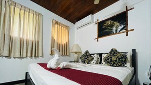 A hotel room with a bed, curtains, a painting, and an air conditioning unit. - Safari Village Hotel (Udawalawa)