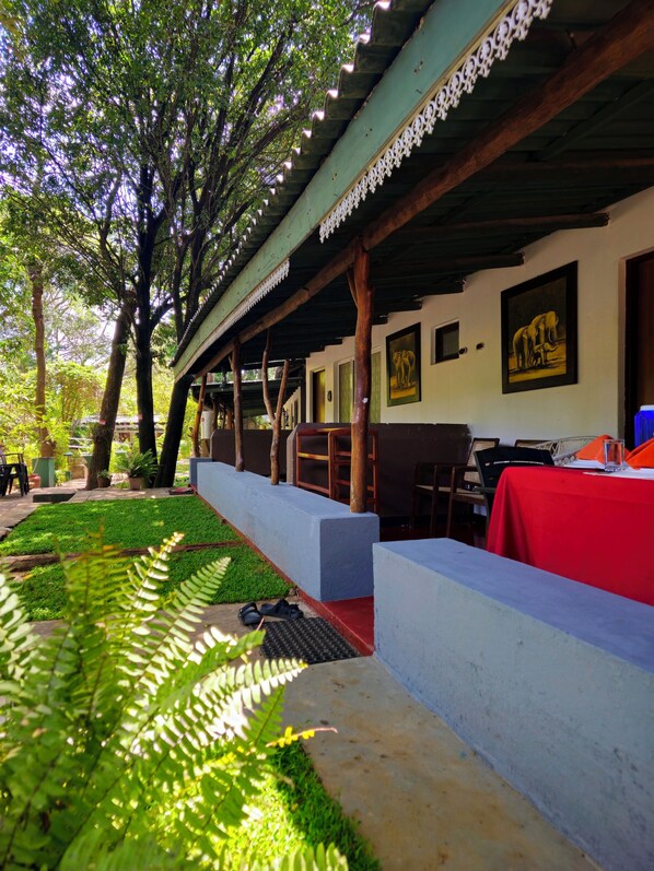 A covered outdoor seating area with tables and chairs, surrounded by greenery and trees. - Safari Village Hotel (Udawalawa)