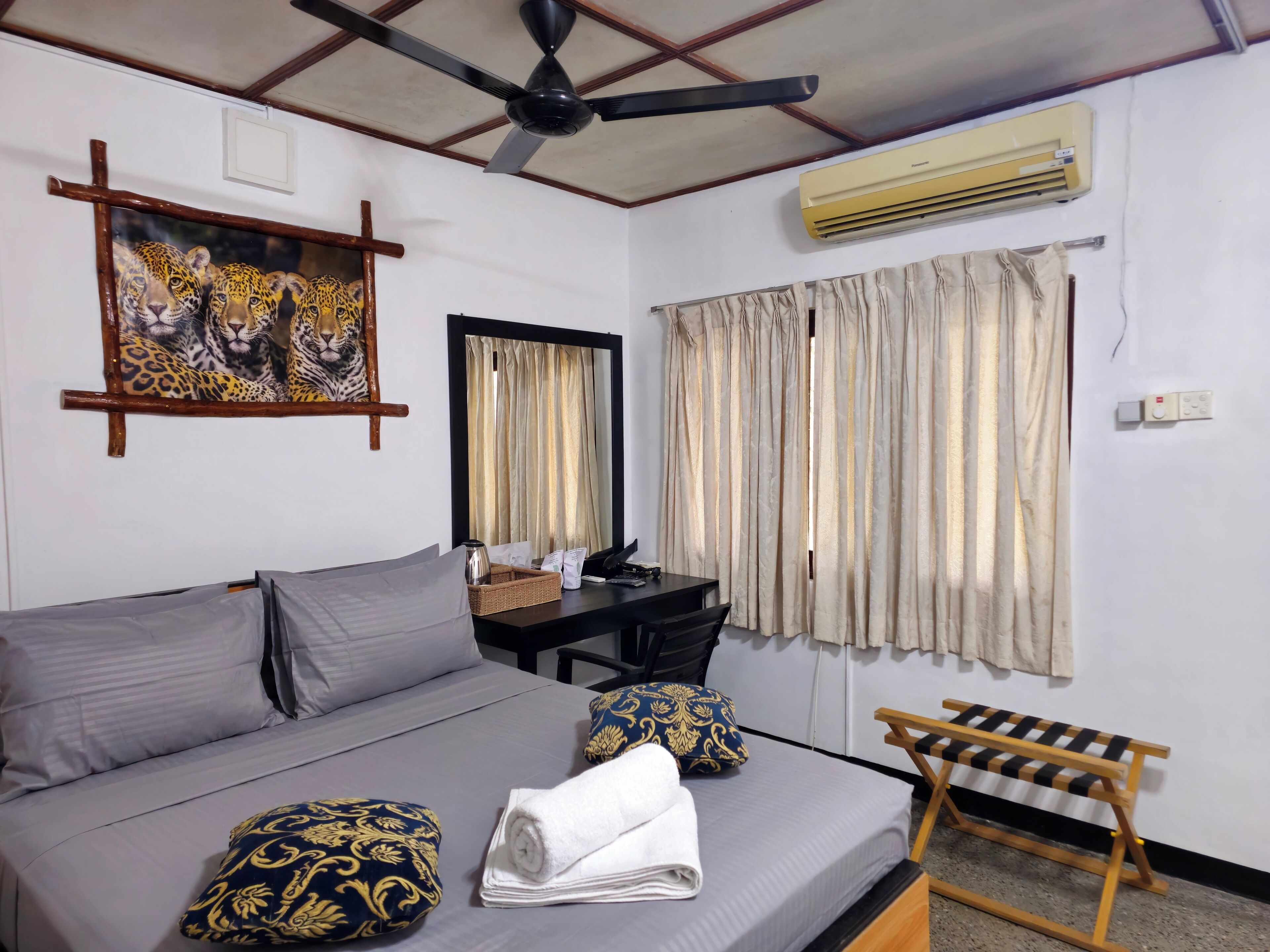 A hotel room with a bed, a desk, an air conditioner, and curtains.