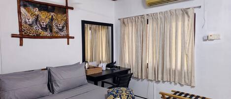 A hotel room with a bed, a desk, an air conditioner, and curtains.
