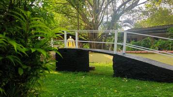A stone bridge over a grassy area with a large tree and a building in the background.