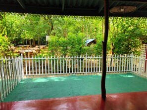 A covered outdoor area with a white fence, green flooring, and lush greenery in the background. - Safari Village Hotel (Udawalawa)