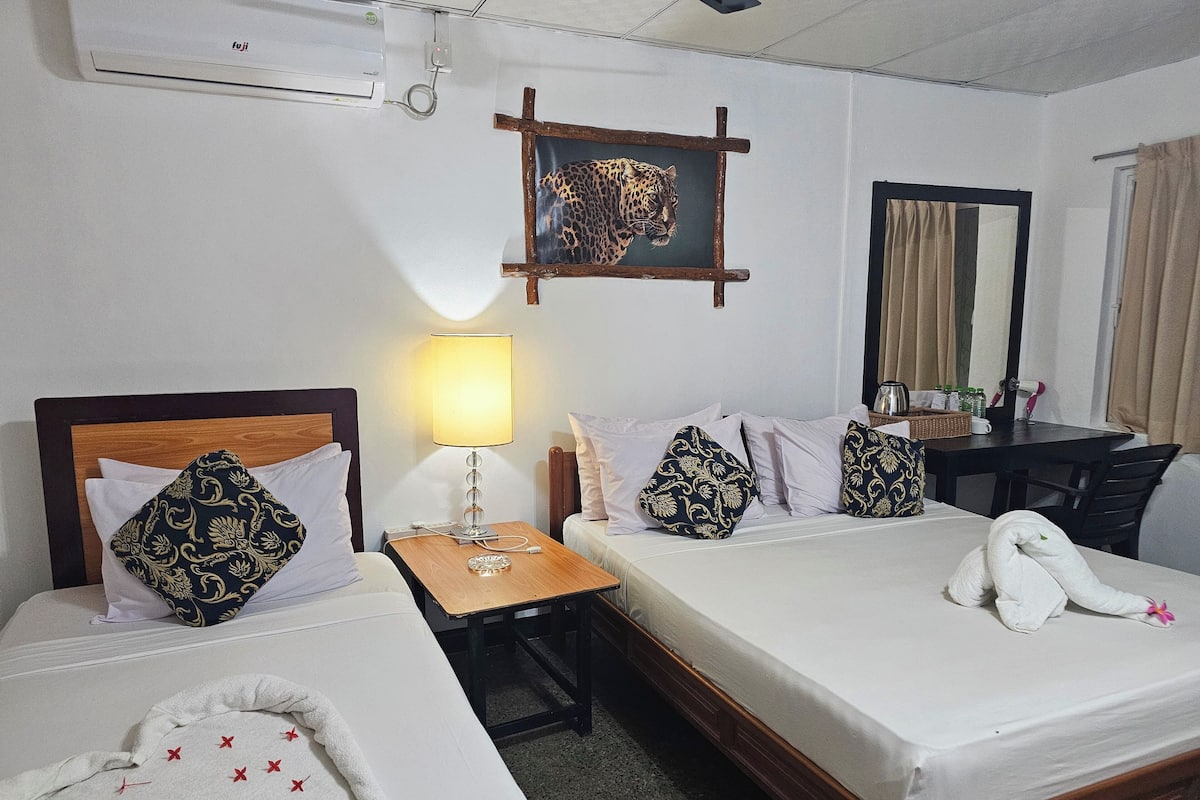 Habitación de hotel con dos camas, cabecera de madera, mesita de noche con lámpara, espejo y una toalla sobre la cama.