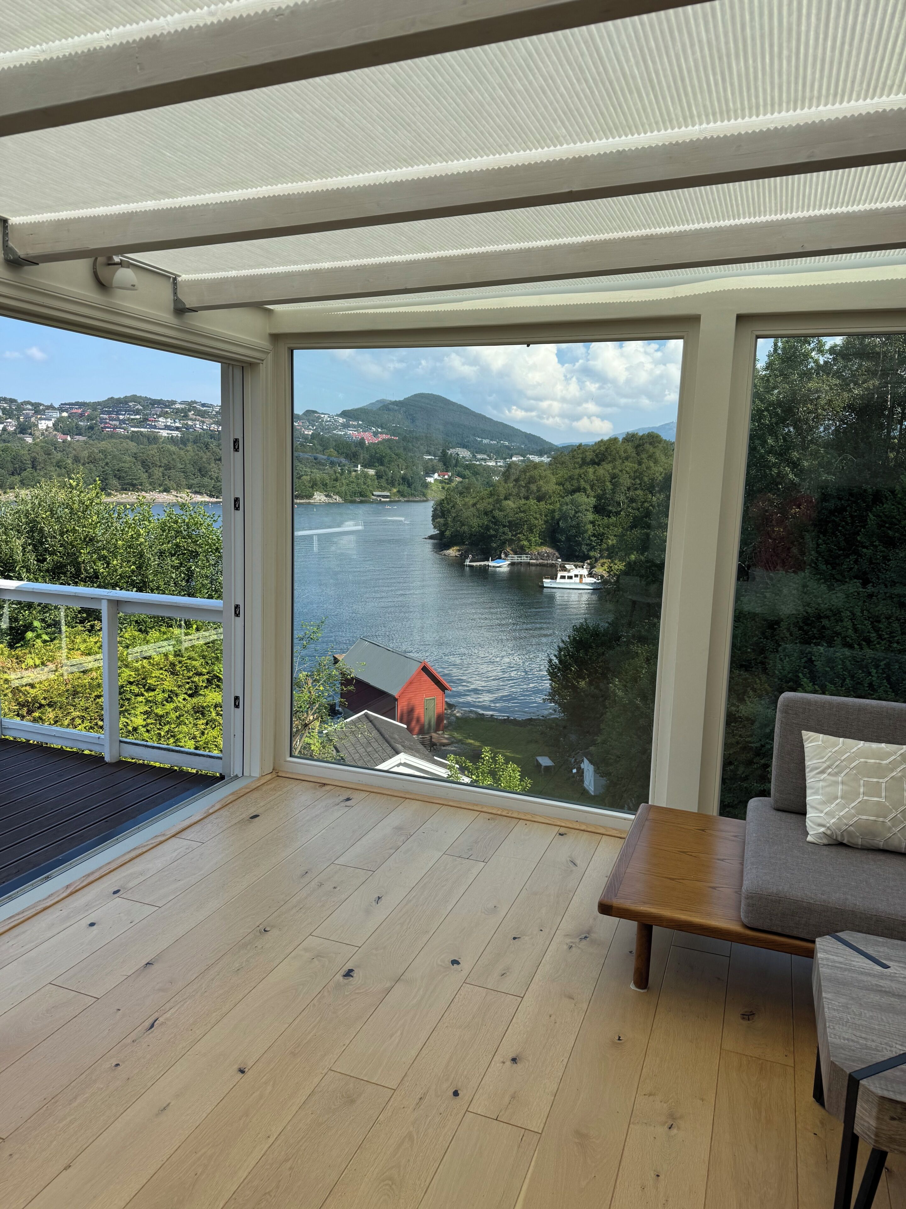 A room with a view of a river, a red building, and a wooden deck.