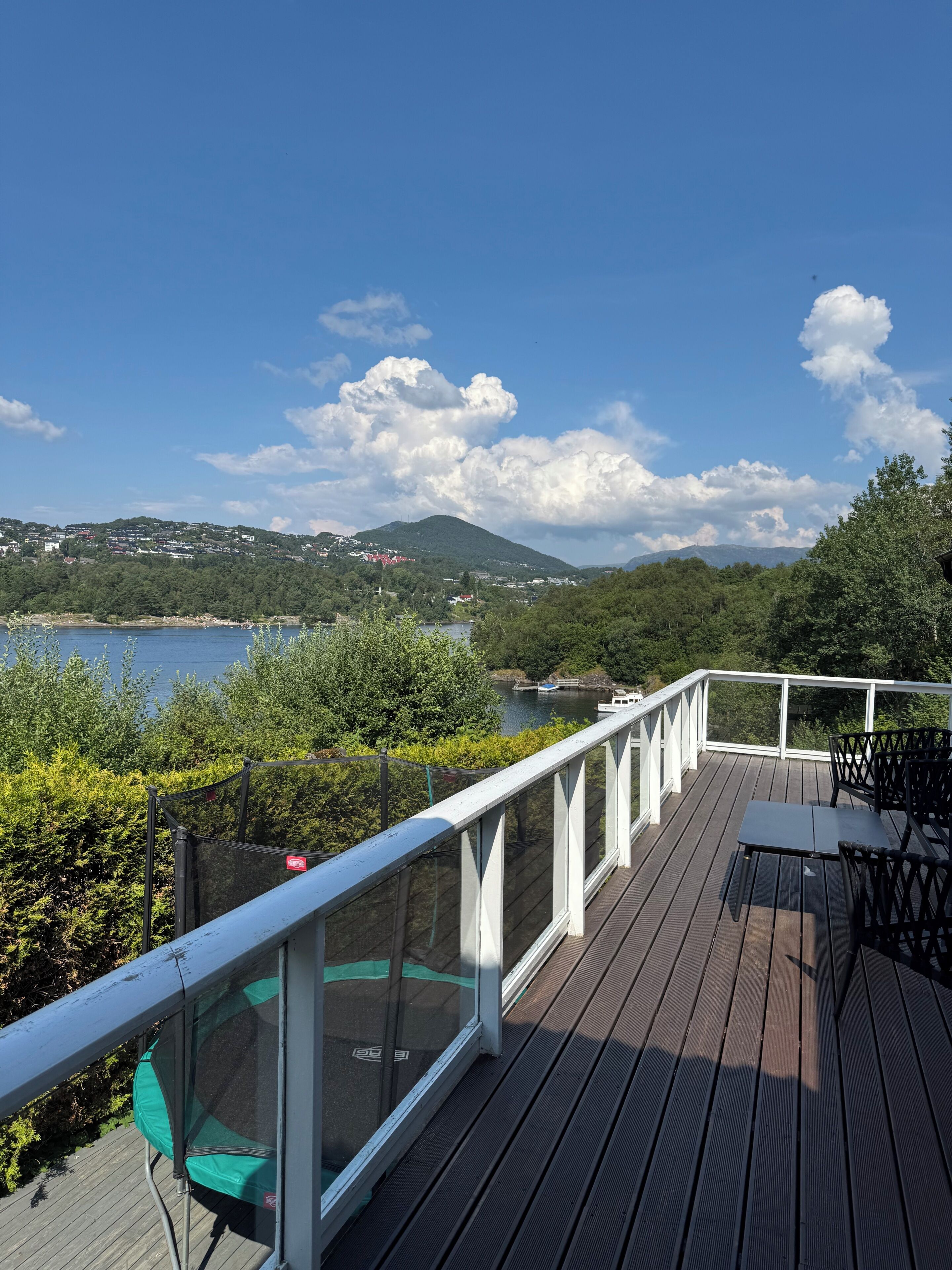 A wooden deck with a glass railing overlooking a lake and hills.