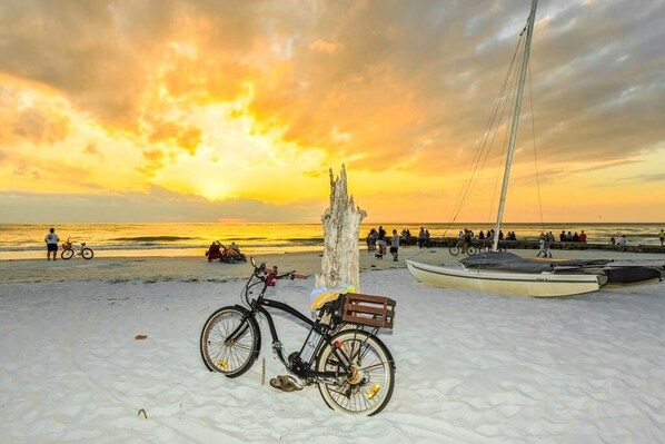 A bicycle parked on a sandy beach with a sunset in the background.
