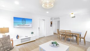 A modern living room with a white color scheme, a dining area with wooden chairs, and a ceiling light fixture.