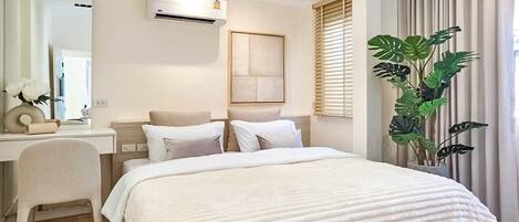 Una habitación de hotel moderna con una cama, un escritorio, un equipo de aire acondicionado, un espejo grande y una planta en maceta.