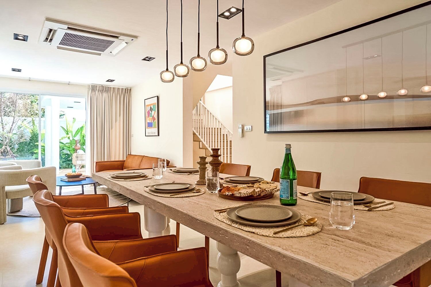 A dining area with a long wooden table set for six, surrounded by orange chairs.