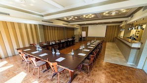 Un salón de conferencias con una larga mesa, sillas, una pantalla de proyector y una zona de cocina.