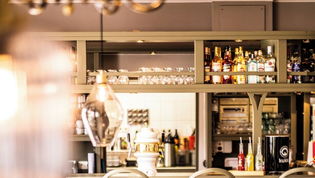 Una zona de bar con mostrador, estanterías llenas de botellas y taburetes.
