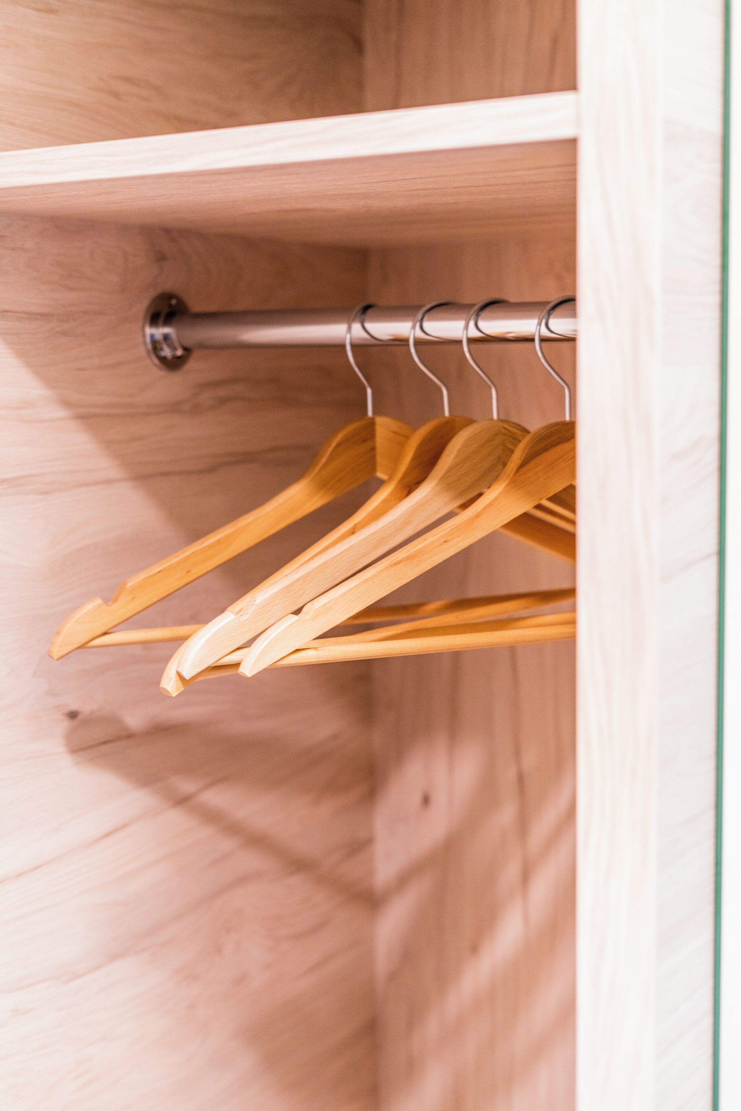 A wooden closet with a metal rod and wooden hangers.