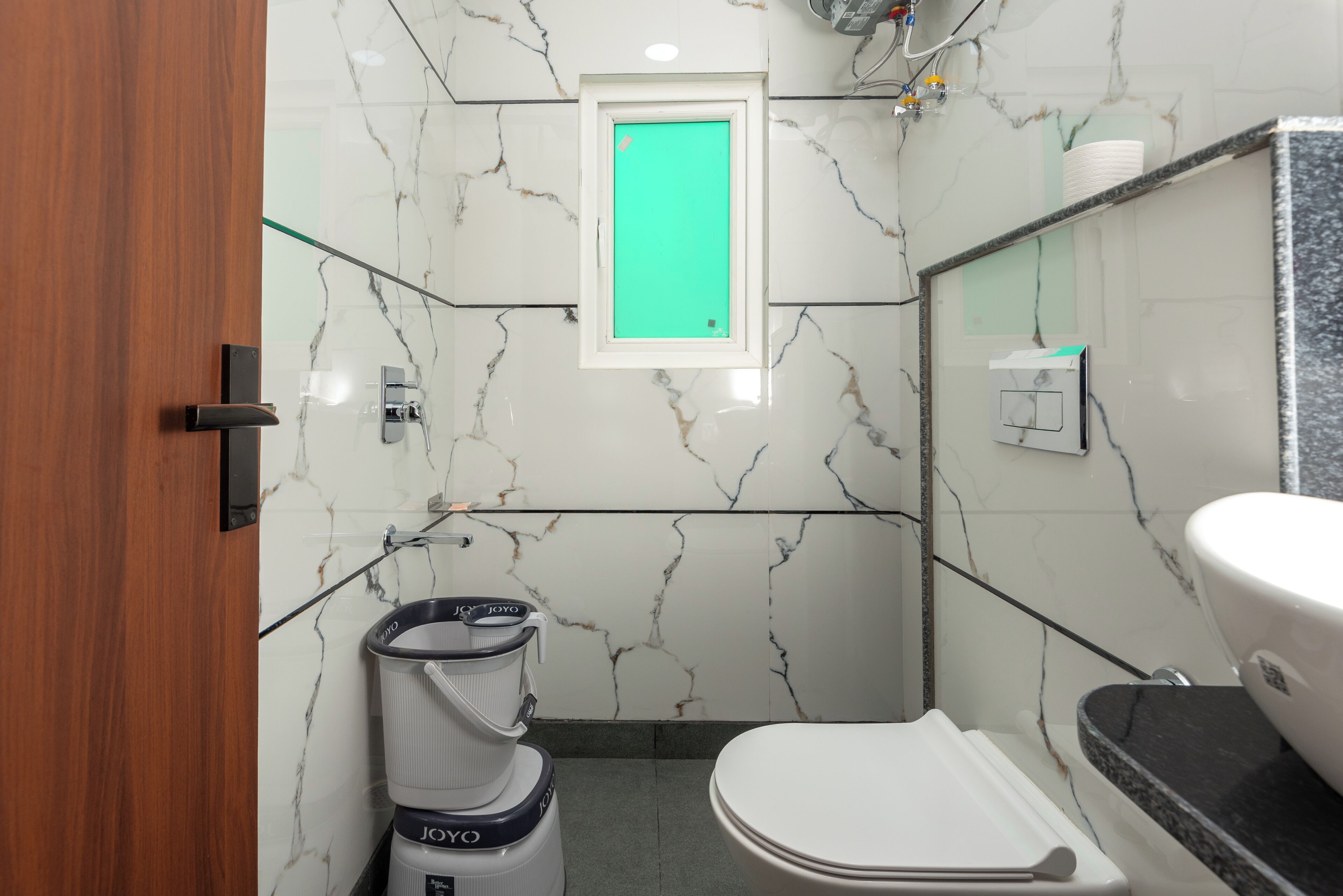 A compact bathroom with a toilet, a small window, and a trash bin.