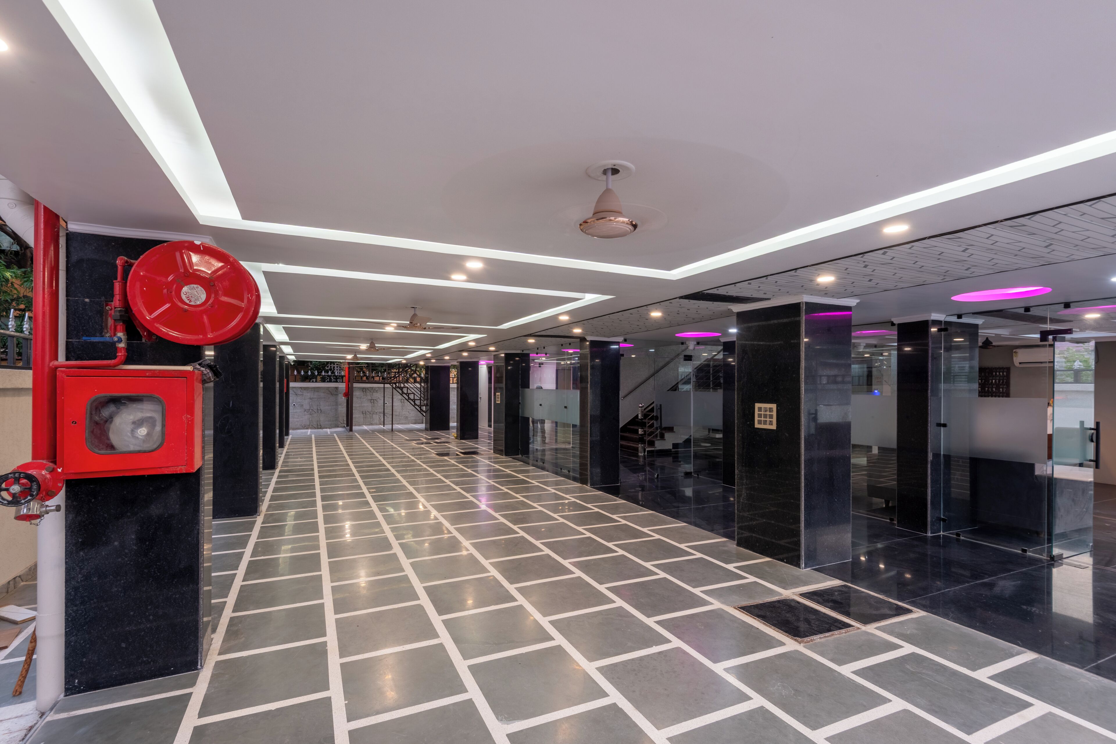 A modern hotel lobby with a tiled floor, a red fire extinguisher, and a staircase.