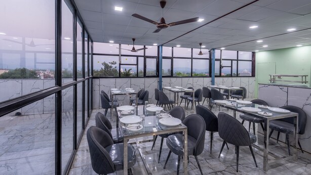 Un área de comedor en la azotea con mesas preparadas para el servicio, amplias ventanas con vistas a la ciudad y ventiladores de techo.
