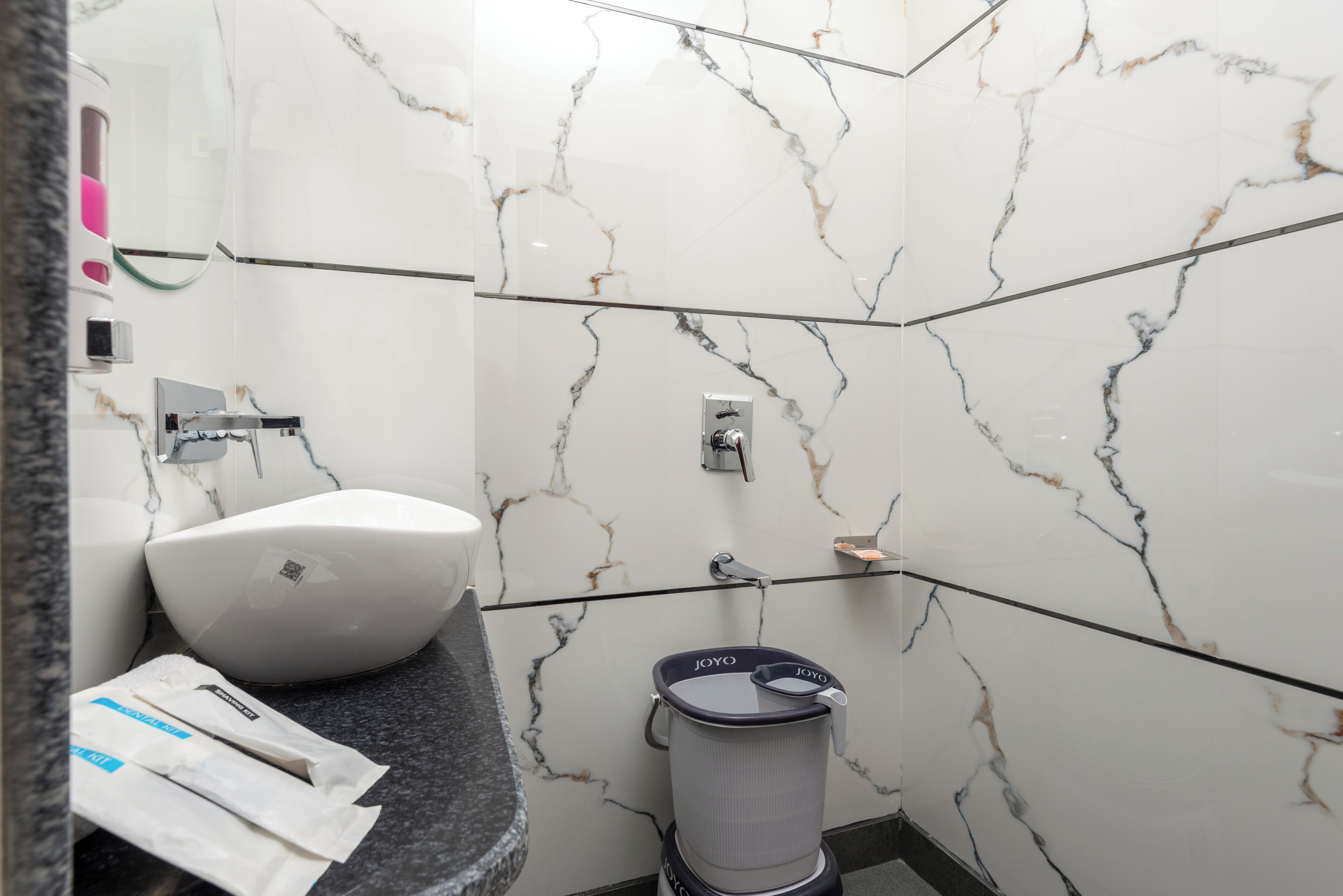 Un baño con lavamanos de mármol blanco, cabina de ducha de vidrio y un inodoro con bidé de la marca Joyo.