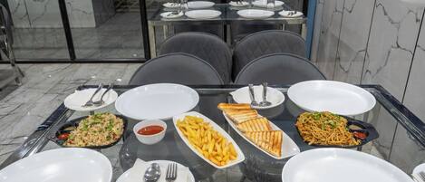 A dining table set with plates, cutlery, and various dishes including fried rice, French fries, grilled sandwiches, and noodles.
