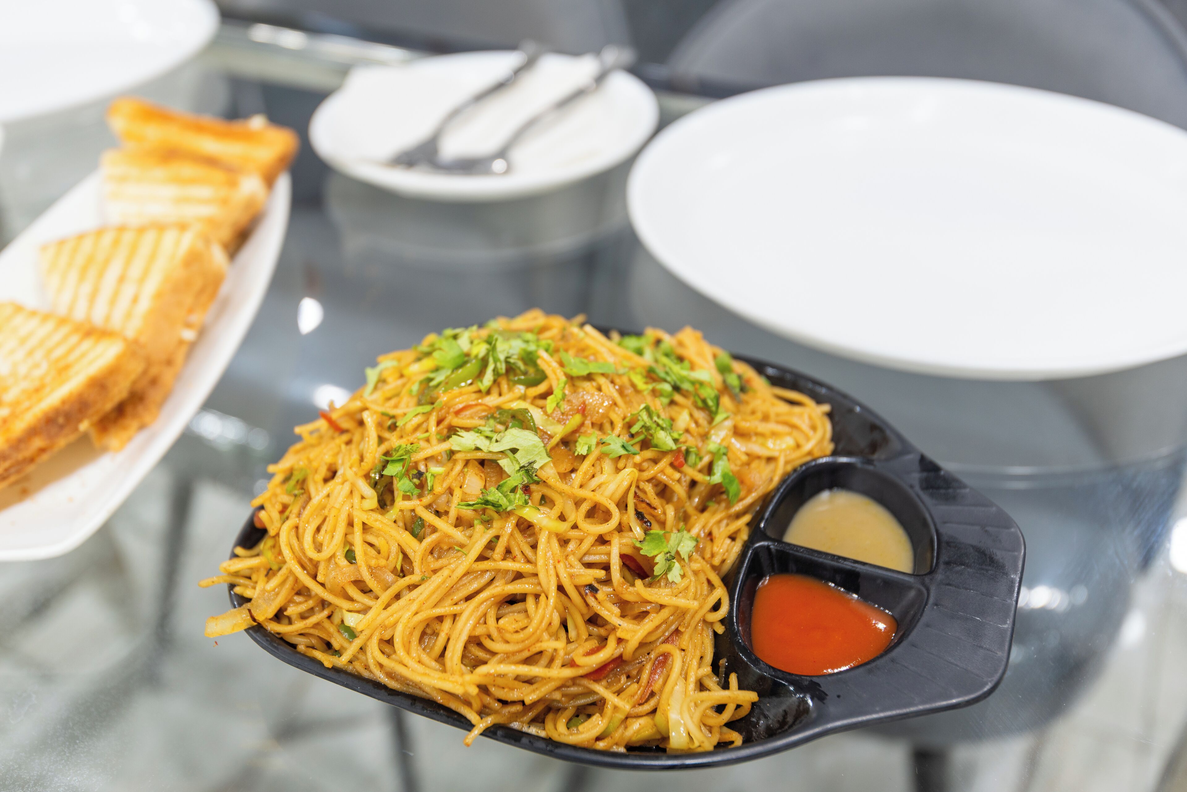 A meal with noodles, a side dish, and a small bowl of sauce.