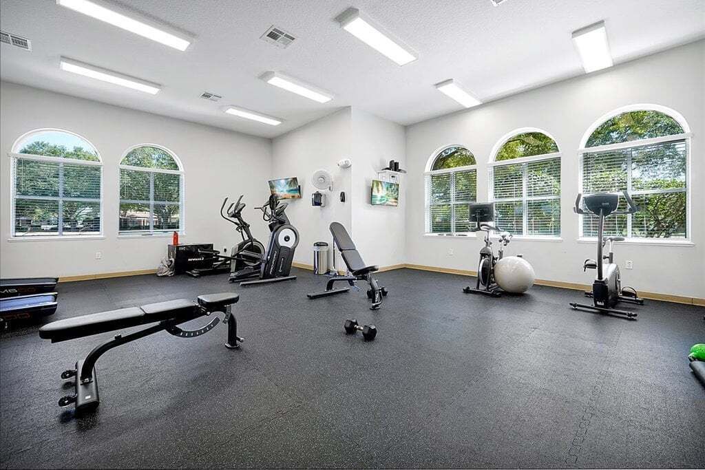 A gym with exercise equipment, large windows, and a bench.