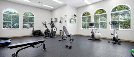 A gym with exercise equipment, large windows, and a bench.