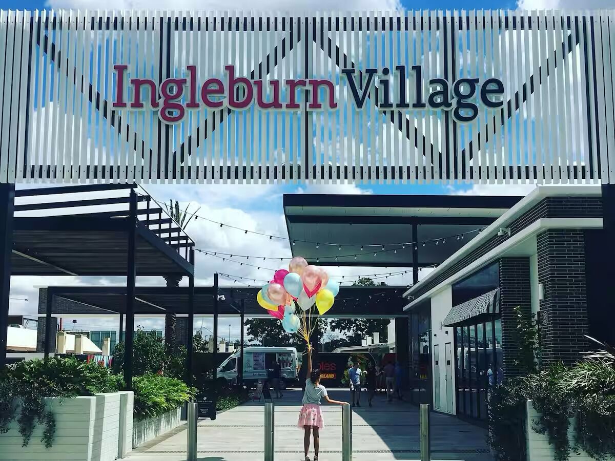 Entrada de um edifício moderno com uma placa indicando 'Ingleburn Village'.
