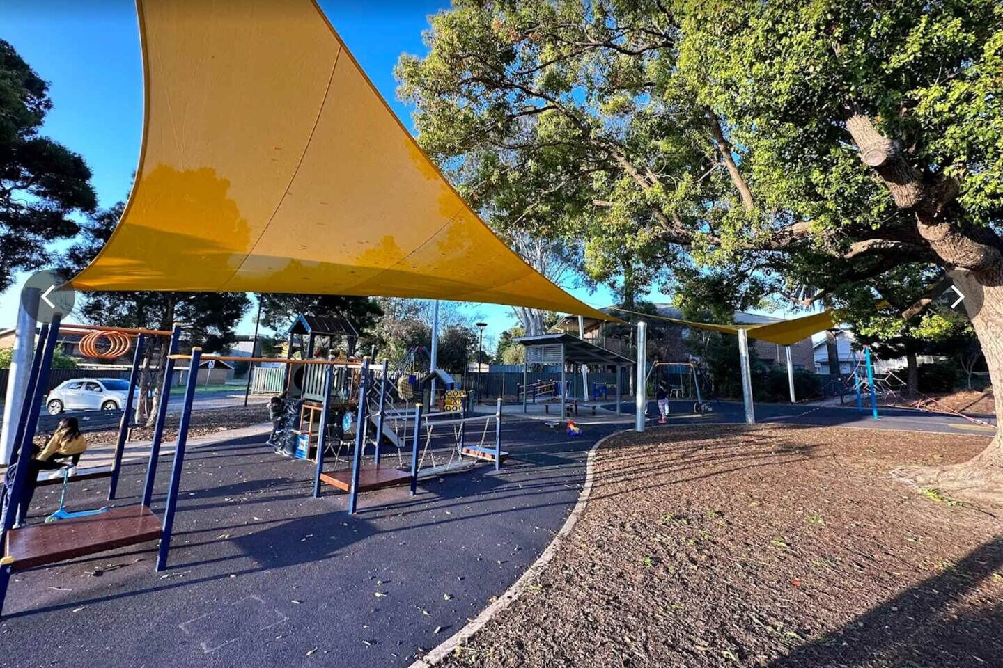 A playground with a yellow shade sail, swings, and climbing structures.