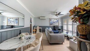 A modern living room with a grey sofa, a marble dining table, and a ceiling fan. - Peaceful 2BR Villa Retreat (Ingleburn)