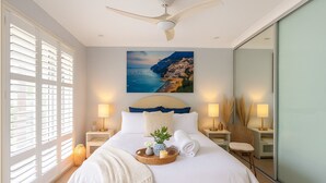 A modern bedroom with a large bed, a ceiling fan, and a scenic painting above the bed. - Peaceful 2BR Villa Retreat (Ingleburn)