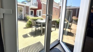 A view through a glass door into a courtyard with a patio table and chairs, a brick building, and a small garden. - Cosy apartment for 5 people with WIFI, TV and terrace (Veere)
