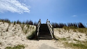 Un escalier en bois menant au sommet d’une dune de sable, avec un ciel dégagé au-dessus.