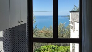 Ein Zimmer mit Meerblick durch ein großes Fenster, einer gefliesten Wand und einem weißen Schrank.