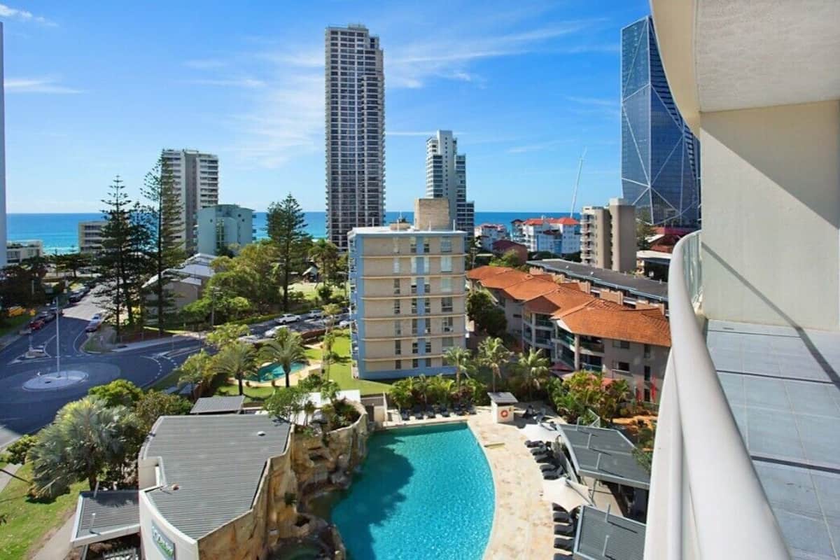 A hotel with a pool, a view of the city, and a beach in the background.
