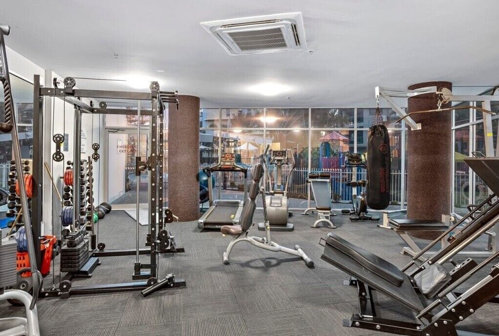 Une salle de sport équipée de divers appareils d’exercice, d’un tapis de course et d’un sac de frappe.