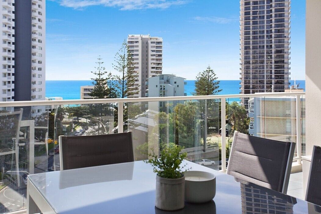 Ein Balkon mit Glasgeländer, der auf eine Stadtlandschaft und das Meer blickt.