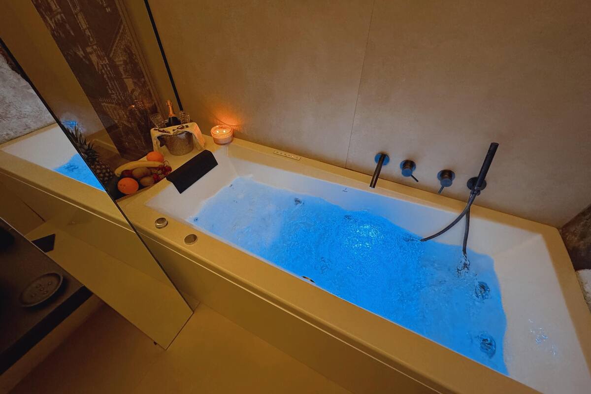 Una bañera con un grifo, una vela y frutas a un lado.