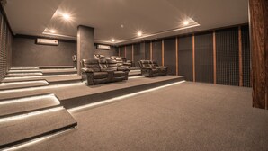 Ein moderner Heimkino-Raum mit Teppichboden, zwei Ledersesseln, einer großen Wand mit Lautsprechern und einer Treppe, die zu einer oberen Ebene führt.