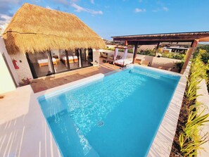 Une piscine dotée d’une structure à toit de chaume et d’un espace salon abrité.