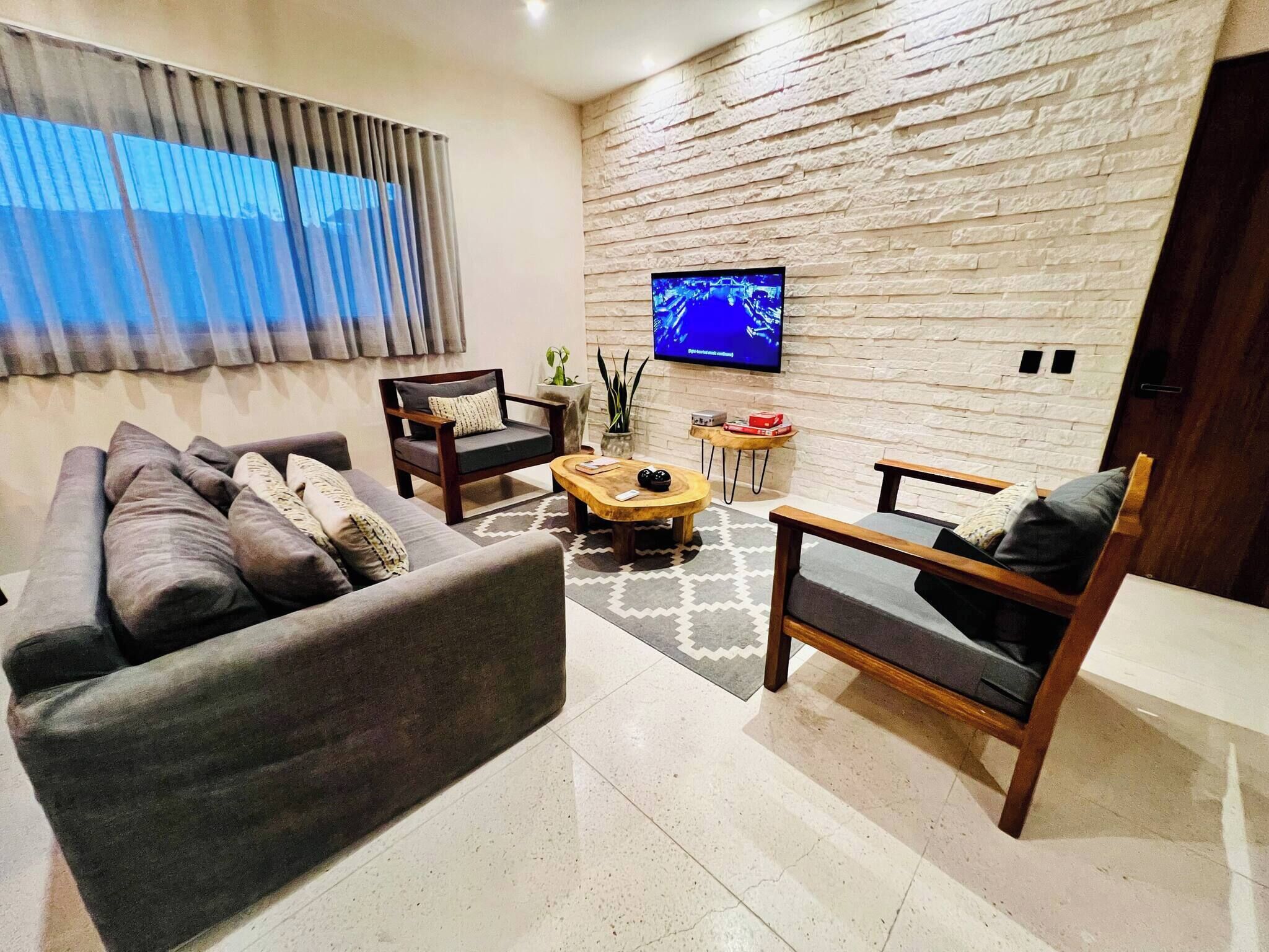 A modern living room with a sofa, armchairs, a coffee table, and a flat-screen TV mounted on a textured wall.