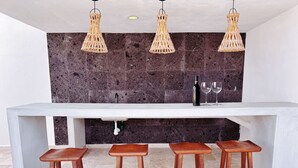Une cuisine avec un plan de travail blanc, trois tabourets en bois et trois suspensions en osier.