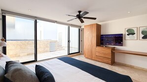 Een slaapkamer met een bed, een televisie, een plafondventilator en een schuifdeur naar een balkon.
