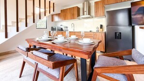 Een moderne keuken met houten kastjes, een roestvrijstalen koelkast en een eethoek met een houten tafel en stoelen.